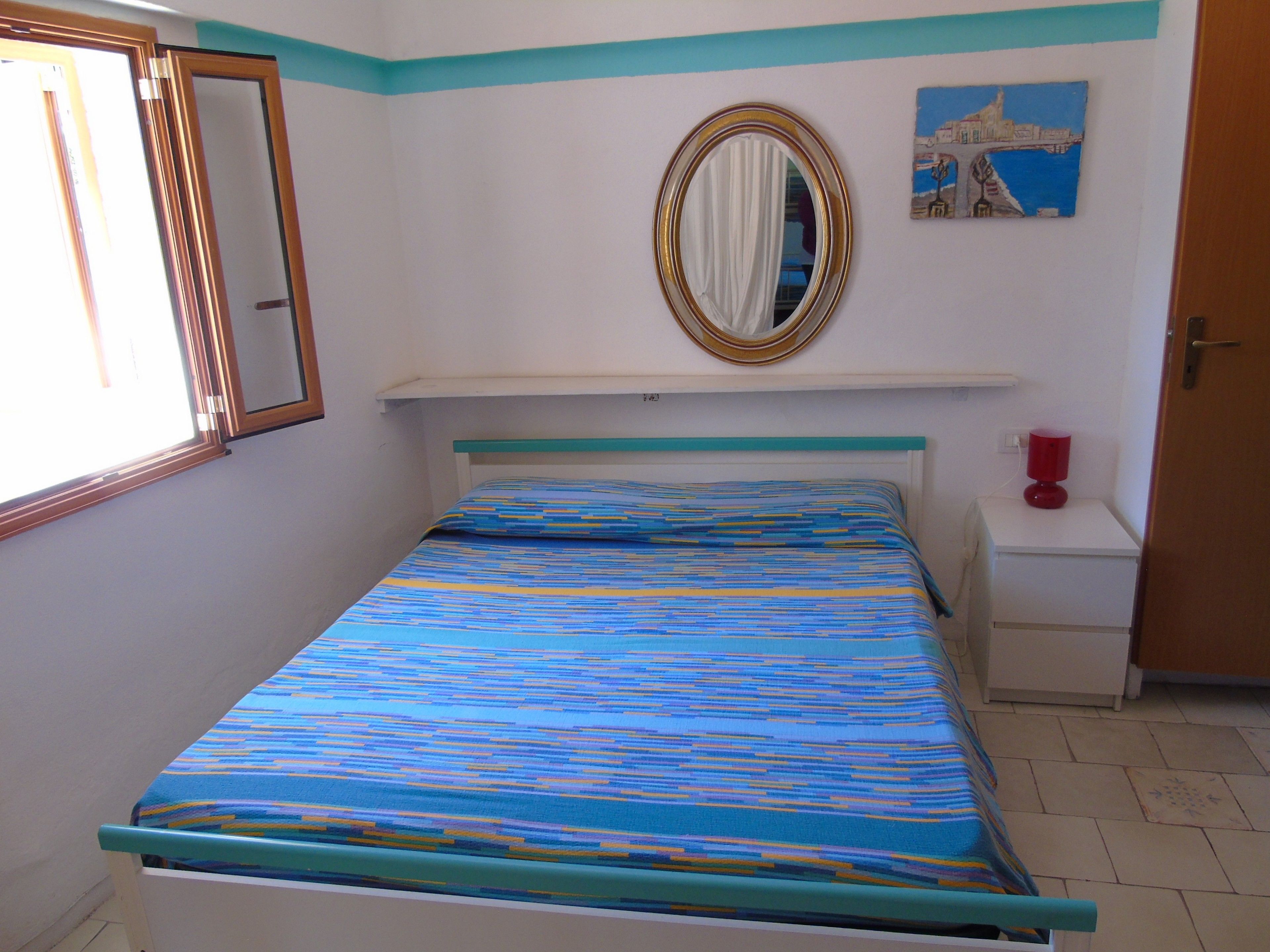 Een slaapkamer met een bed, nachtkastje, spiegel en een schilderij aan de muur.