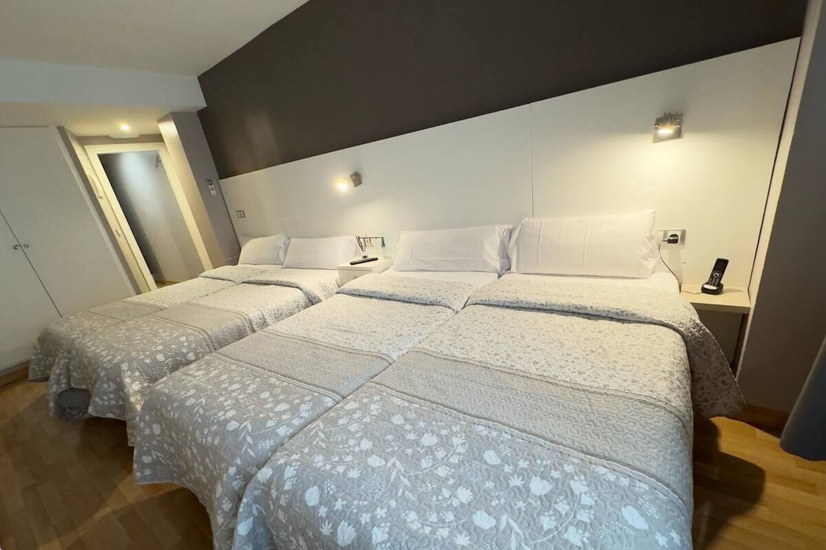 Un dormitorio con una cama grande, dos mesitas de noche y un velador con un teléfono.
