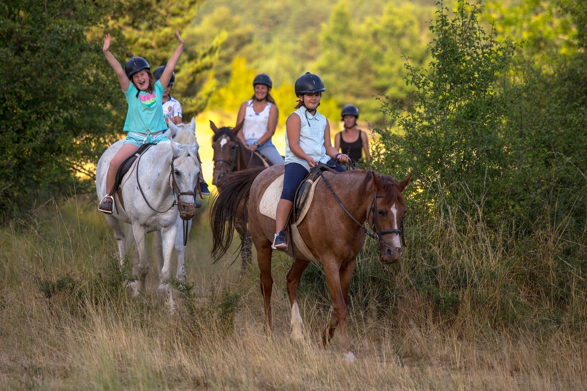Tres personas montando caballos en un área con césped y árboles al fondo.