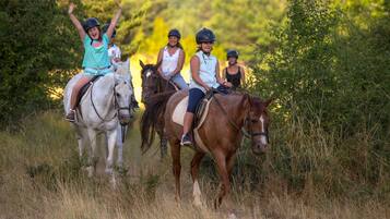 Tres personas montando caballos en un área con césped y árboles al fondo.