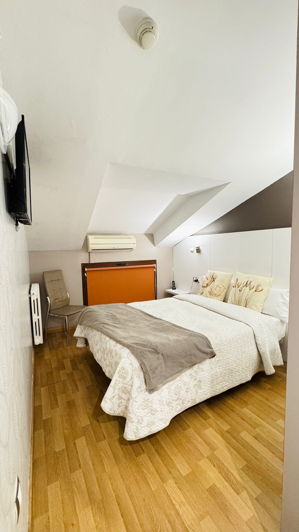 Una camera da letto con un letto, una sedia, un comodino, un condizionatore d'aria e una TV a parete.