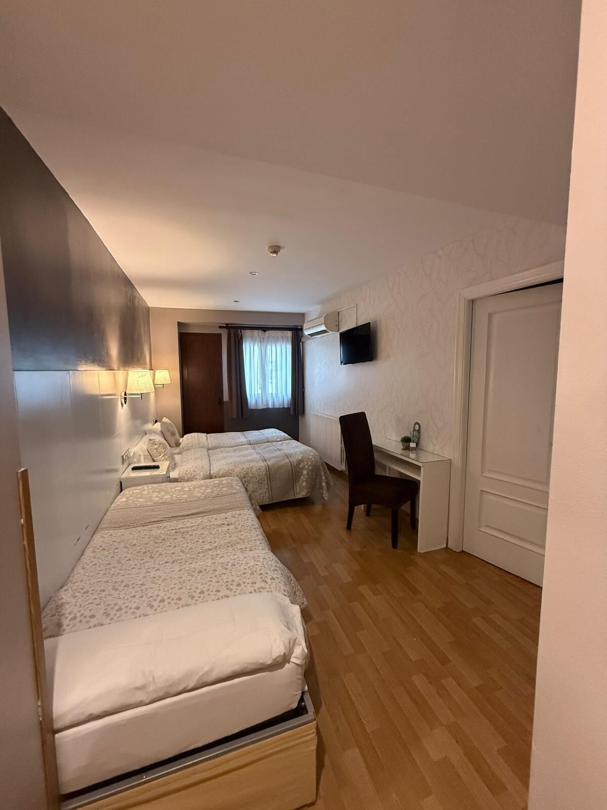 A hotel room with two beds, a desk, a chair, a TV, and a door.