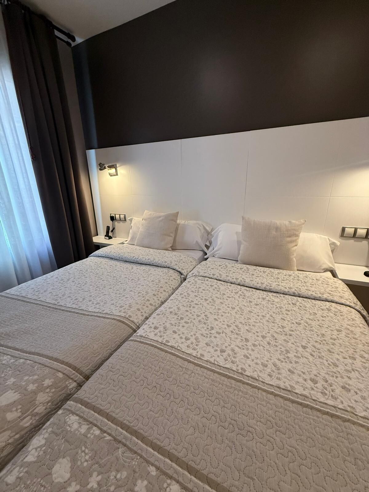 A double bed with a patterned bedspread, a dark headboard, and bedside lamps.