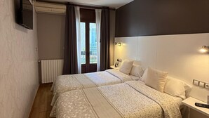 Un dormitorio con cama, mesita de noche, lámpara y televisor montado en la pared.