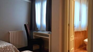 Ein Hotelzimmer mit zwei Betten, einem Schreibtisch, einem Stuhl, einer Klimaanlage und Blick ins Bad durch eine offene Tür.