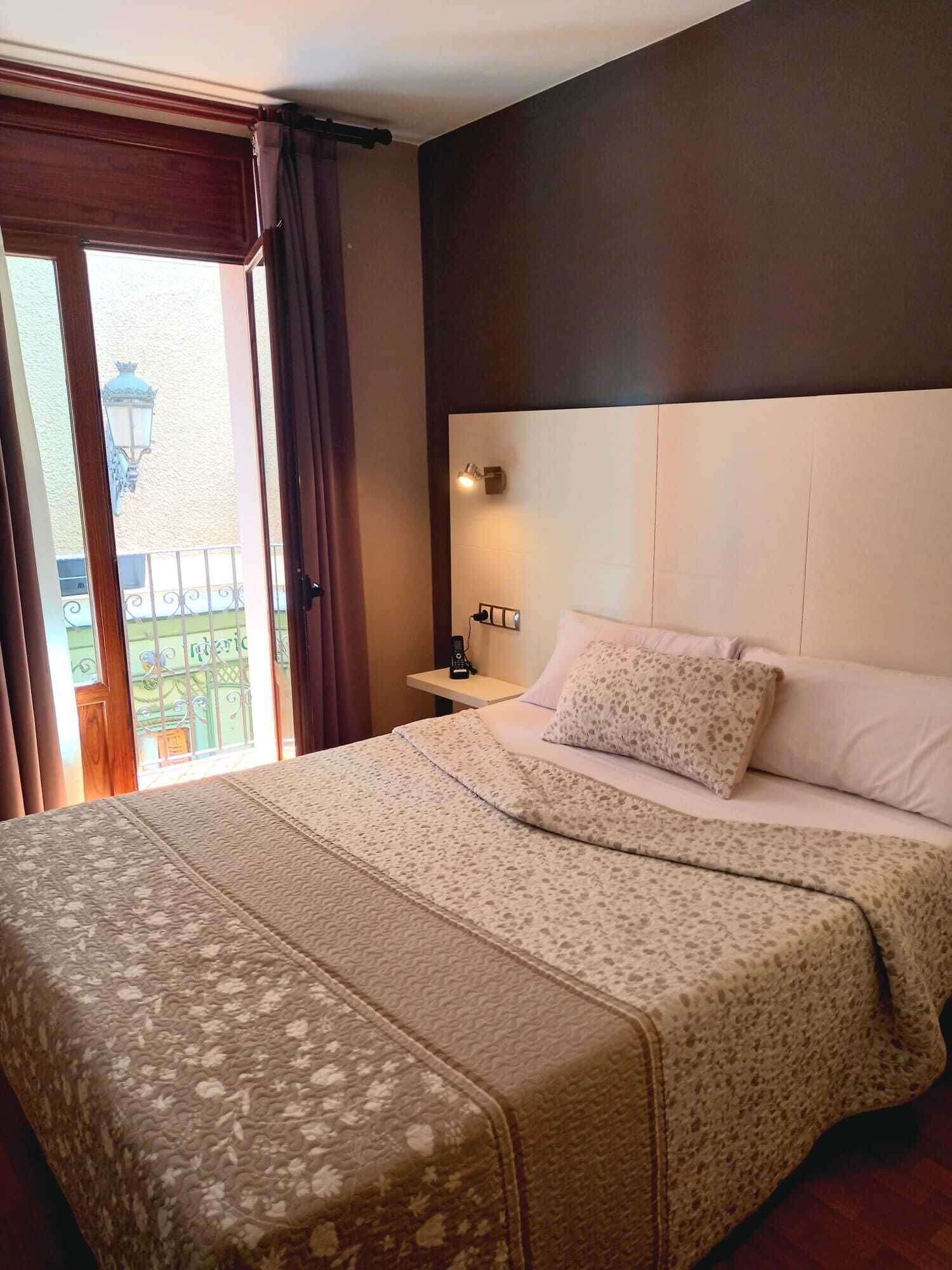 Quarto de hotel com uma cama grande, mesa de cabeceira, luminária na parede e vista para uma varanda.