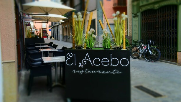 Un área de estar al aire libre con mesas y sillas, un cartel que dice 'El Acebo Restaurante' y una bicicleta estacionada cerca.
