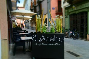 An outdoor seating area with tables and chairs, a sign for 'El Acebo Restaurante', and a bicycle parked nearby. - Hotel El Acebo (Jaca)
