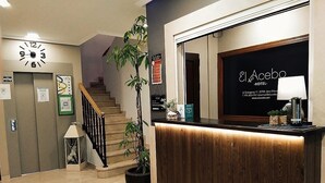 Zona de recepción de hotel con un mostrador de madera, un reloj y una escalera.