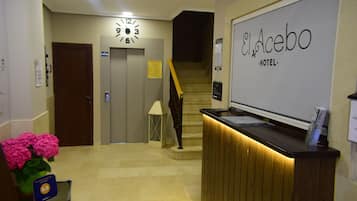 En hotellobby med en receptionsdisk, en klocka och en trappa.
