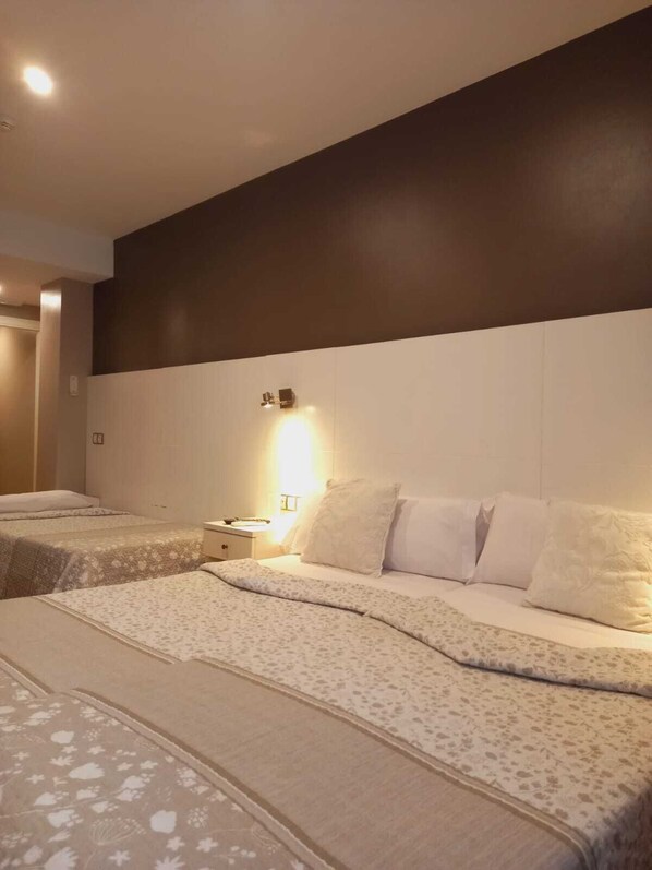A hotel room with two beds, each with a floral-patterned bedspread and white pillows. There is a nightstand with a lamp between the beds. - Hotel El Acebo (Jaca)