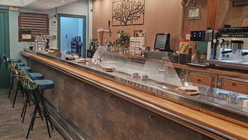 A modern bar area with a long counter, stools, and a coffee machine.