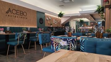 Interior de restaurante con asientos tapizados en azul, mesas de madera y un letrero en la pared que dice 'ACEBO restaurant lounge'.