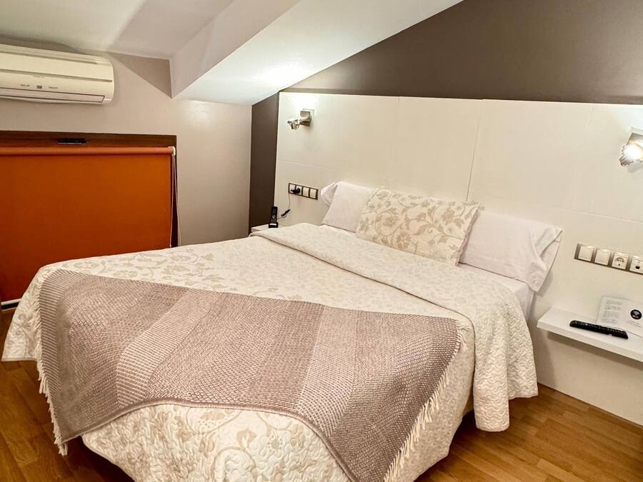 A bedroom with a bed, a nightstand, a wall-mounted light, and an air conditioning unit.