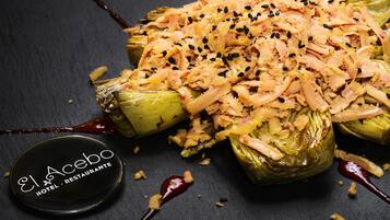 Un plato de alcachofas rellenas, queso rallado y semillas de sésamo negro, sobre un plato de pizarra oscura.