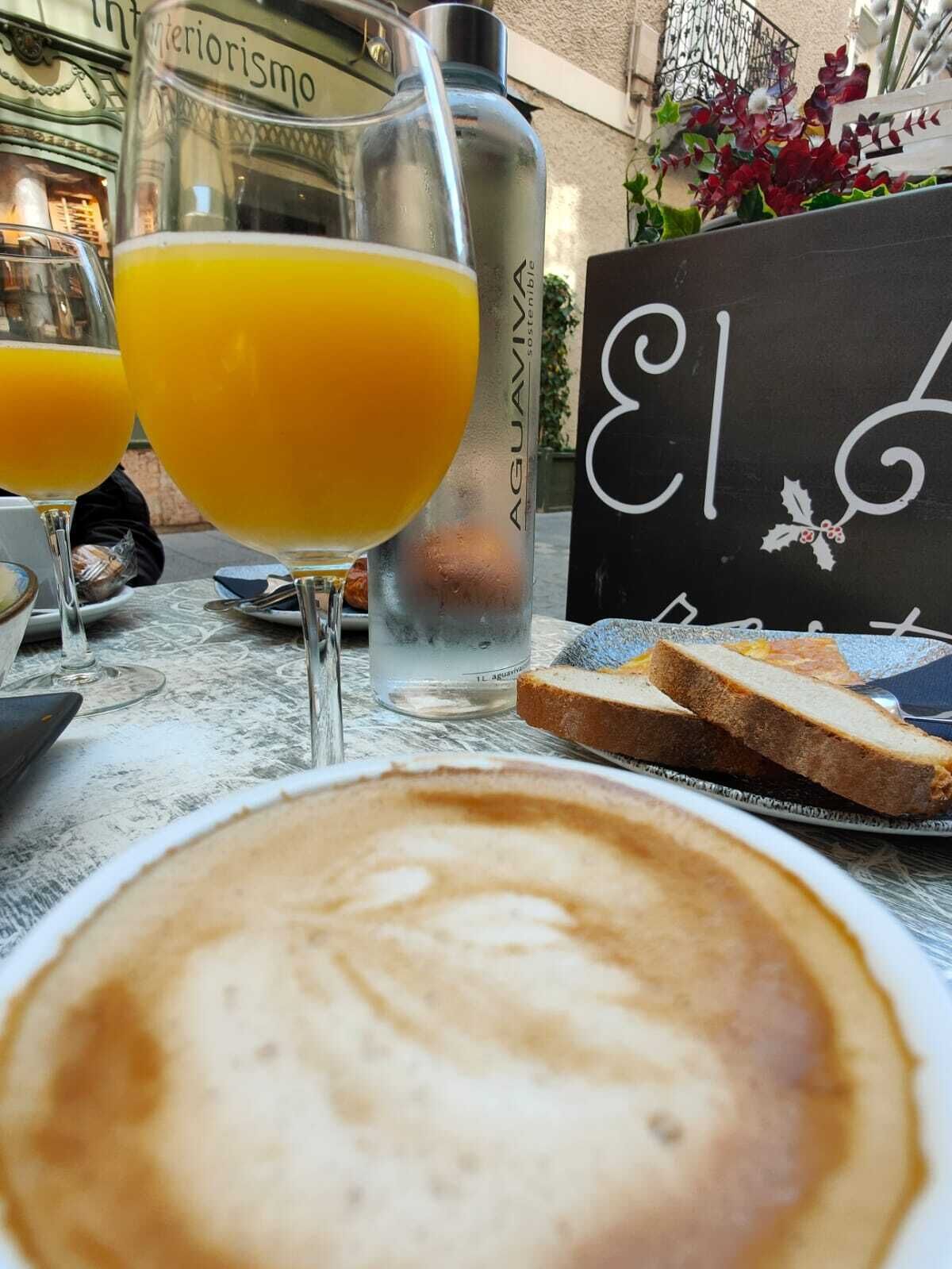 Una mesa con un capuchino, dos vasos de jugo de naranja, una botella de agua y un cartel con un número.