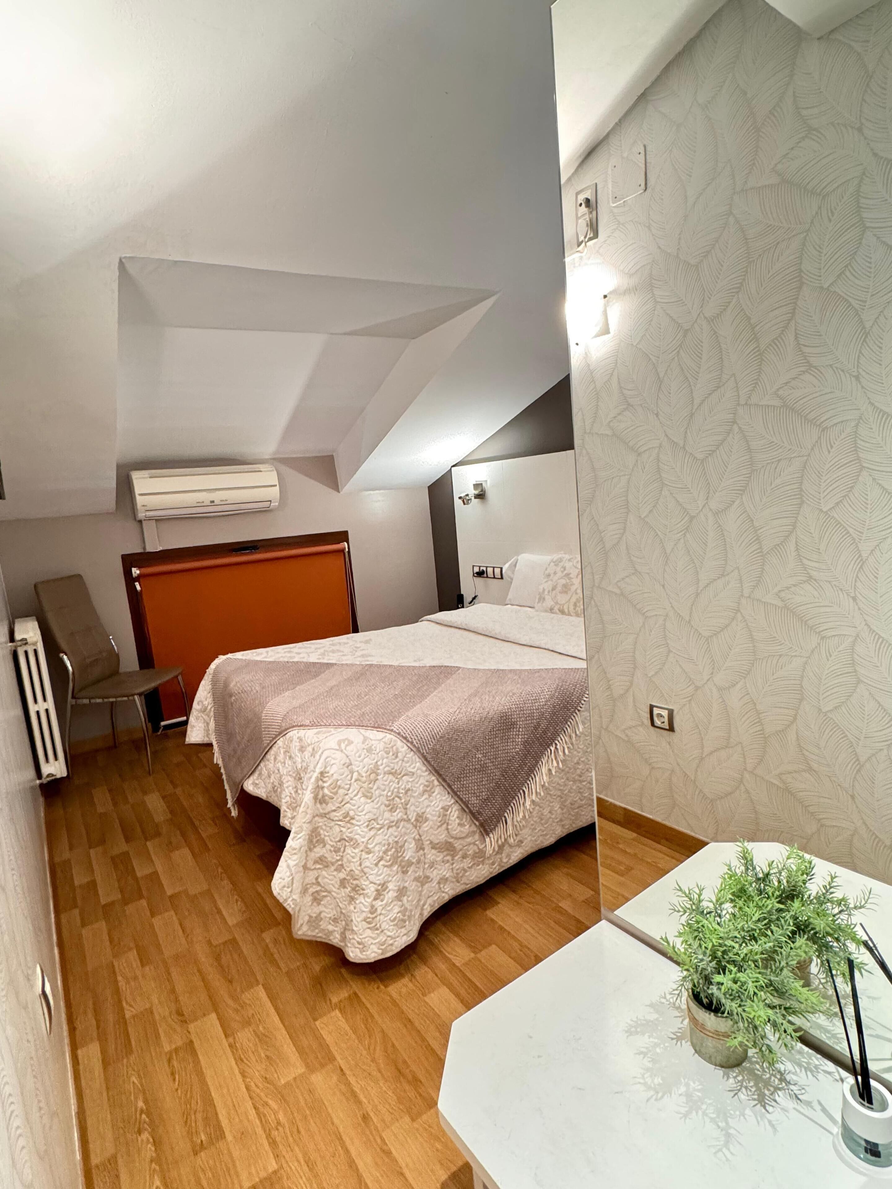 A bedroom with a bed, a chair, a radiator, a ceiling fan, and a potted plant.