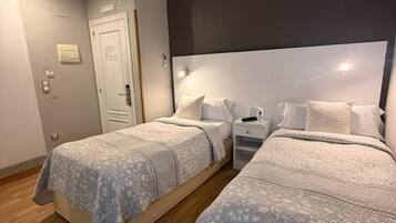 Una habitación de hotel con dos camas, una mesita de noche, una puerta blanca y un termostato en la pared.