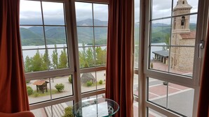Una habitación con amplios ventanales que ofrecen vistas a un lago, montañas y una torre histórica.