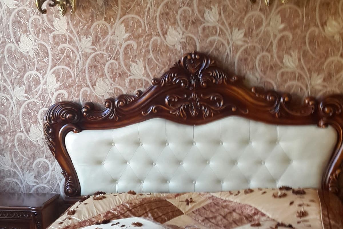 A bedroom with a tufted headboard, floral patterned bedding, and wall sconces.
