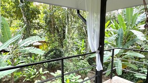 A balcony with a view of lush greenery, a tiled floor, and a hanging light fixture. - El Jardin de Playa Negra (Cahuita)