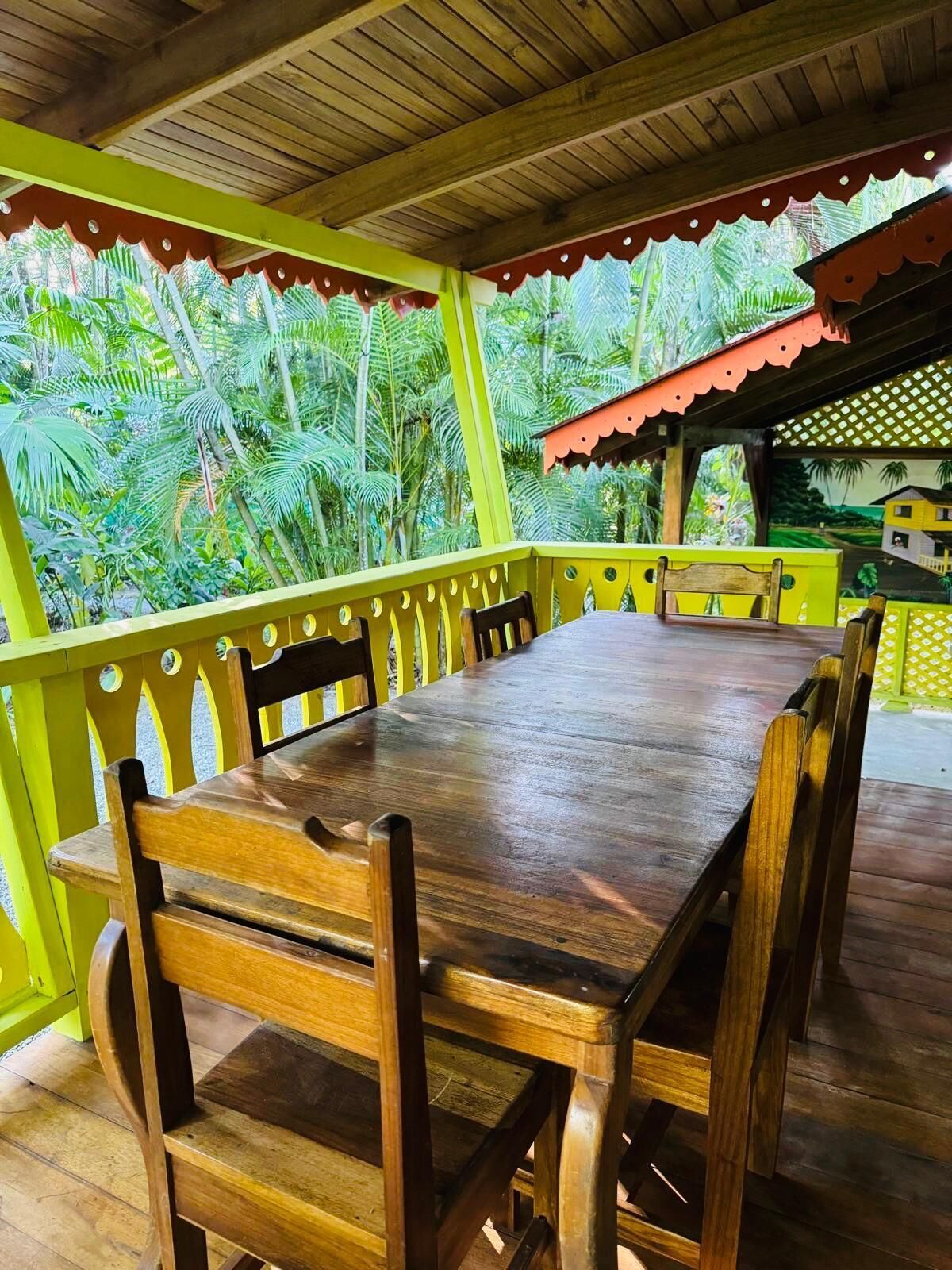 A wooden table with chairs in a covered outdoor area with a view of lush greenery.