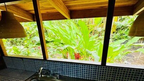 A kitchen with a sink, blue tiled backsplash, and a window overlooking a garden. - El Jardin de Playa Negra (Cahuita)