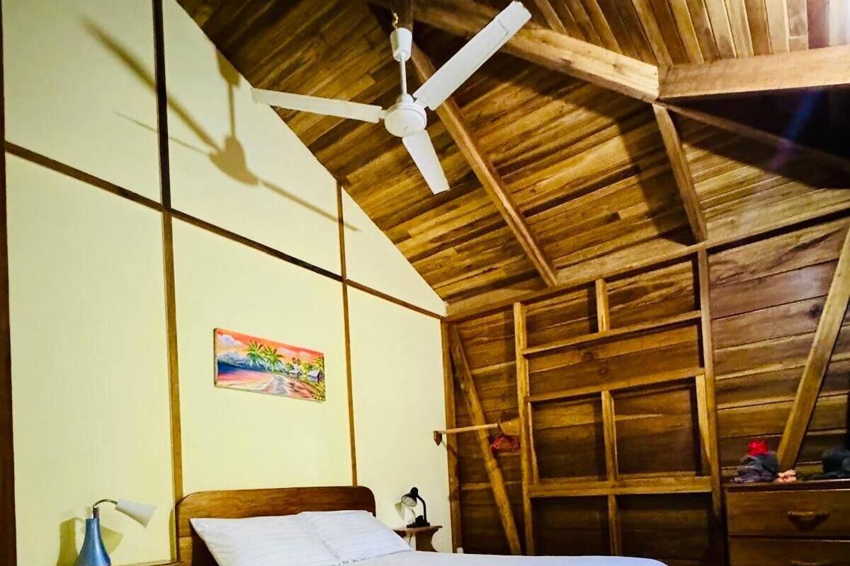 Quarto de madeira com cama, ventilador de teto e um quadro na parede.
