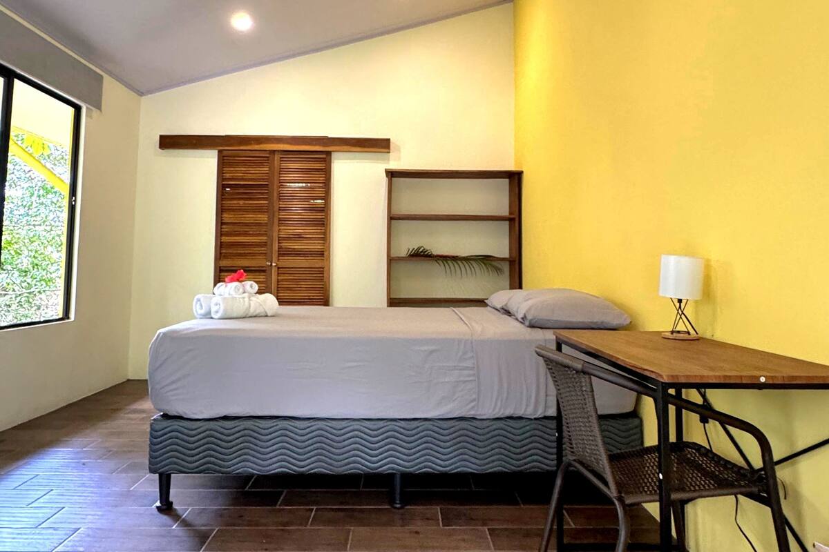 Quarto com cama, escrivaninha, cadeira, ventilador de teto e janela.