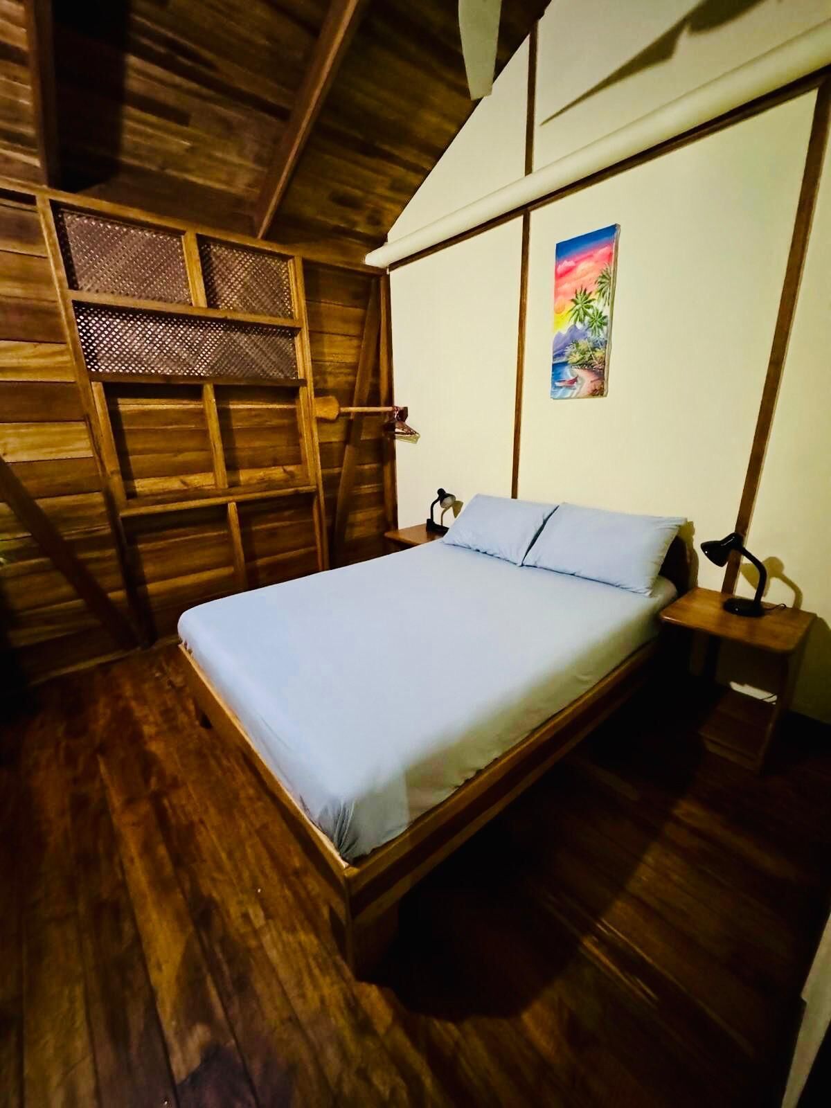 A wooden room with a bed, a ladder, and a painting on the wall.