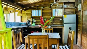 A wooden interior with a dining table and chairs, a refrigerator, and a window. - El Jardin de Playa Negra (Cahuita)
