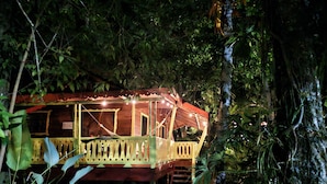 A wooden treehouse with a wooden deck and a staircase leading up to it, surrounded by dense foliage. - El Jardin de Playa Negra (Cahuita)