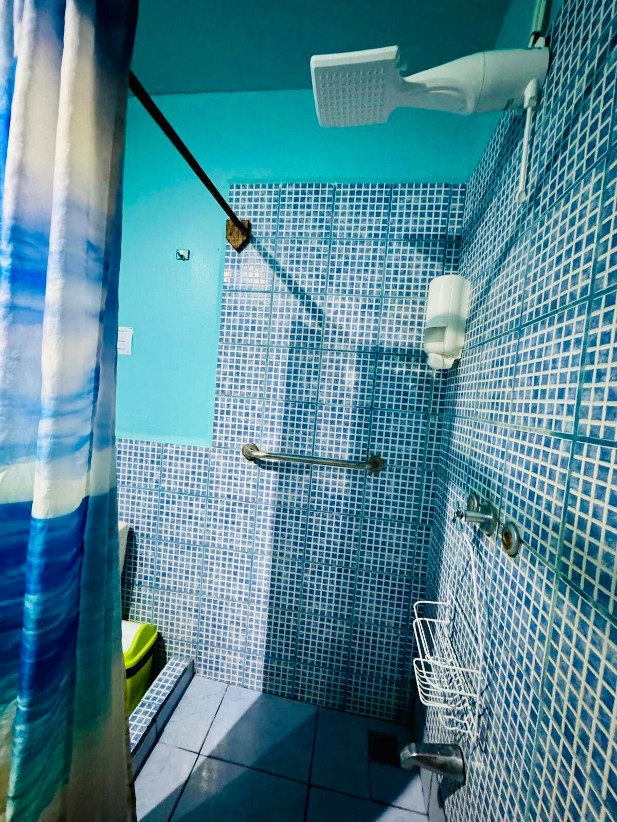 Un baño con azulejos de mosaico azules, un cabezal de ducha, un perchero para toallas y un secador de manos.