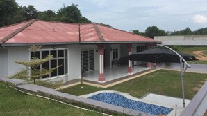 Uma casa com telhado vermelho, piscina e varanda coberta.