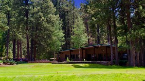 A lodge with a covered porch and a grassy lawn, surrounded by tall pine trees. - Pendaries Village Lodge (Rociada)