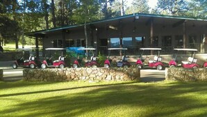 A building with a stone wall in front, a covered area with tables, and several golf carts parked in front. - Pendaries Village Lodge (Rociada)