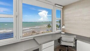 Een kamer met uitzicht op het strand en de zee, door grote ramen.