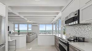 Een moderne keuken met een centraal eiland, grote ramen en uitzicht op zee.
