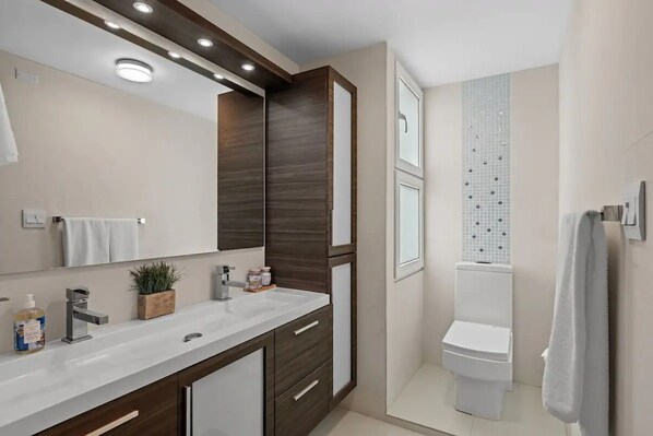 Un baño moderno con un espejo grande, un lavabo blanco, armarios de madera oscura y un inodoro.