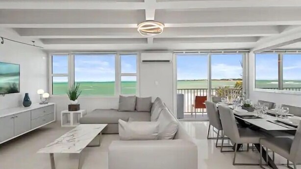 Een moderne woonkamer met een groot raam, een eethoek en een balkon met uitzicht op zee.