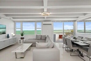 Una sala de estar moderna con un ventanal grande, un comedor y un balcón con vistas al mar.