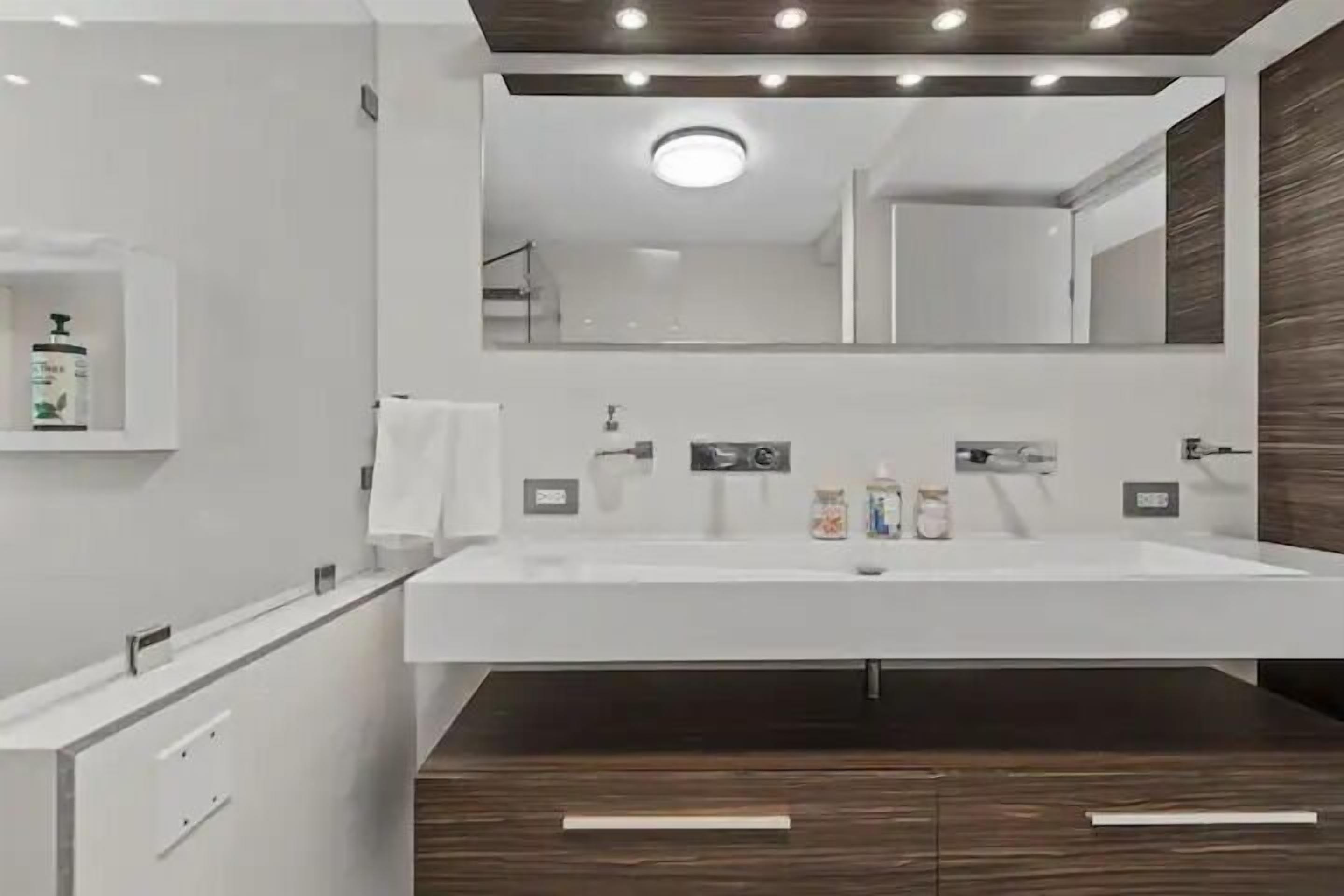 A modern bathroom with a large mirror, white sink, and dark wood cabinets.