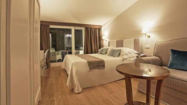 A hotel room with a bed, a sofa, a wooden table, and a view of the outdoors. - Bergamo Inn (Bergamo)