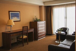Habitación de hotel con escritorio, silla, sofá y una pequeña mesa con una planta.