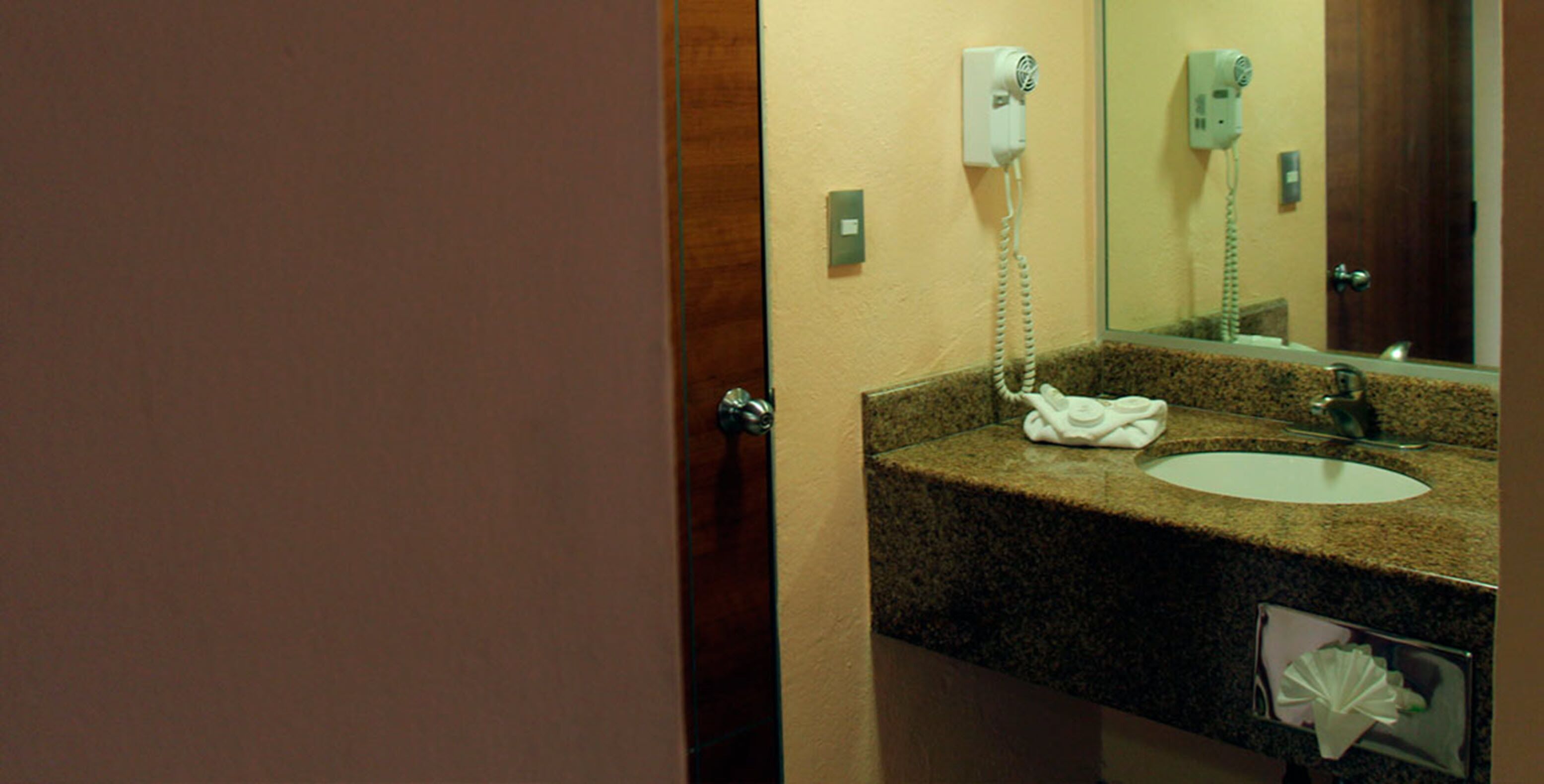 A bathroom with a granite countertop, a sink, a mirror, and a towel rack.