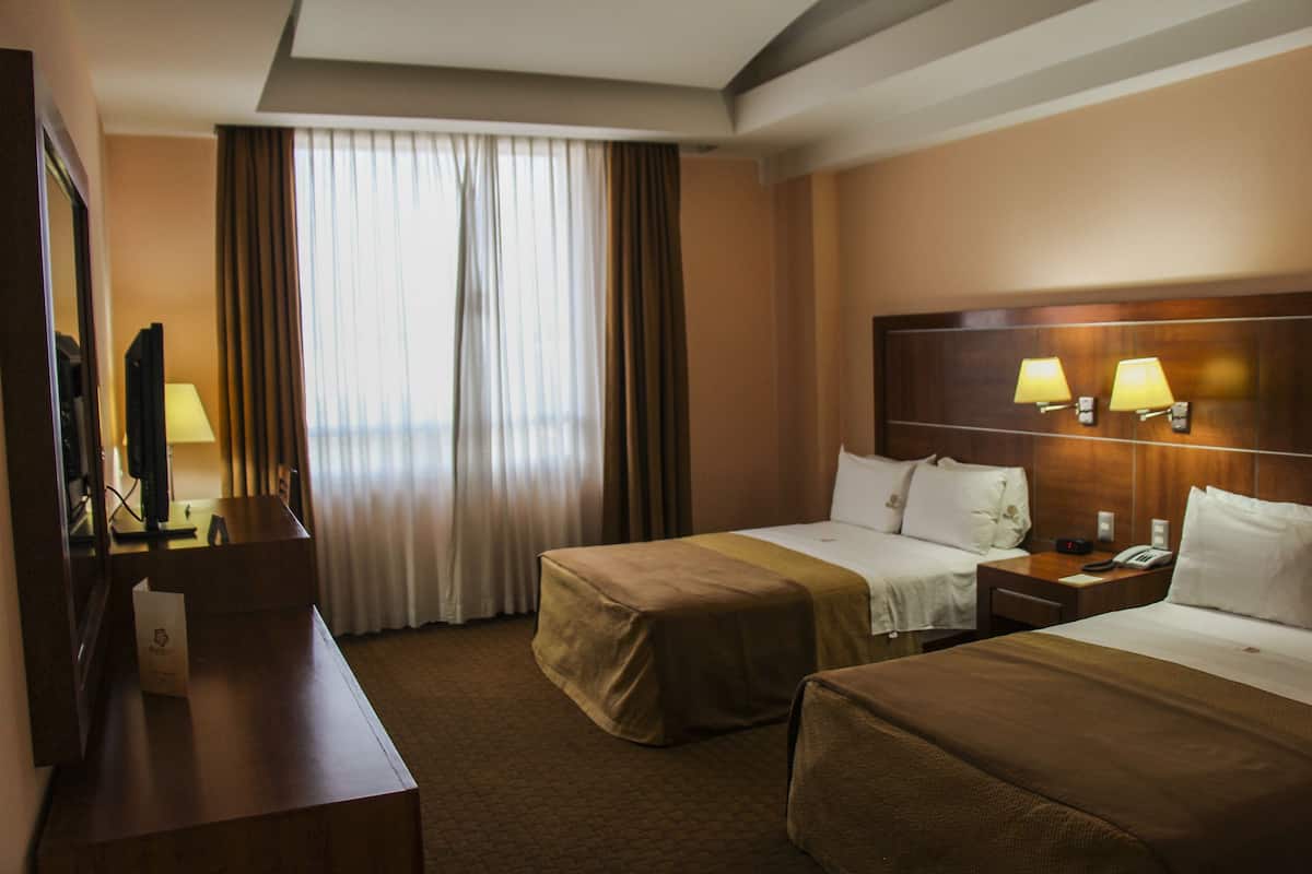 Habitación de hotel con dos camas, un escritorio, un televisor y una ventana con cortinas.
