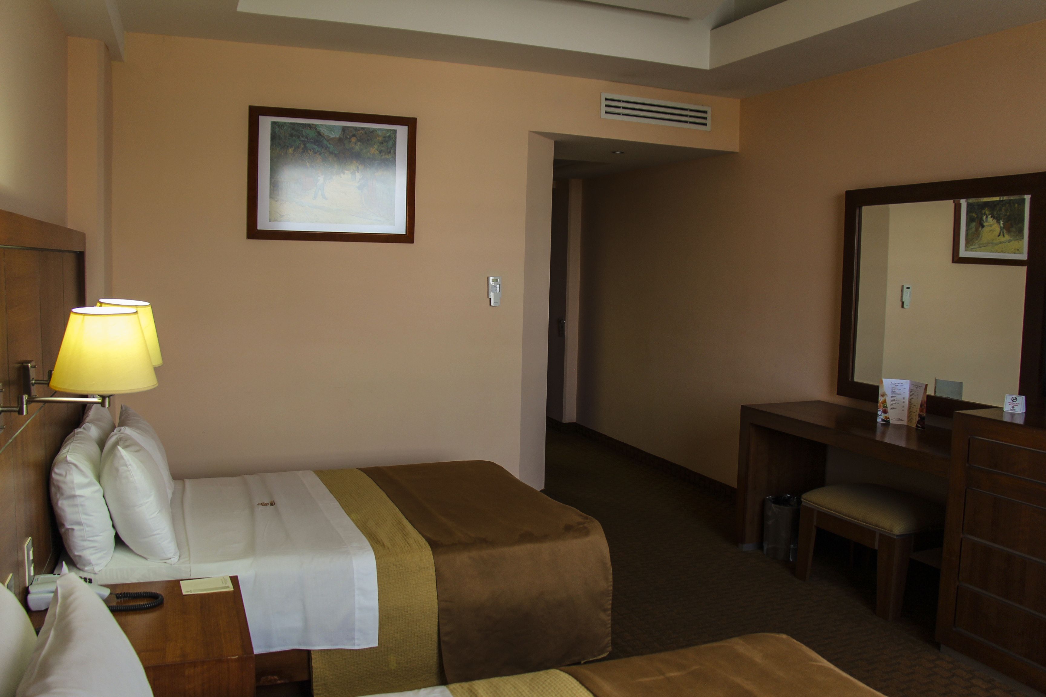 Ein Hotelzimmer mit einem Bett, einem Nachttisch, einer Lampe und einem Schreibtisch mit Stuhl.