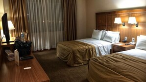 Une chambre d’hôtel avec deux lits, un bureau en bois, une télévision et une fenêtre avec des rideaux.