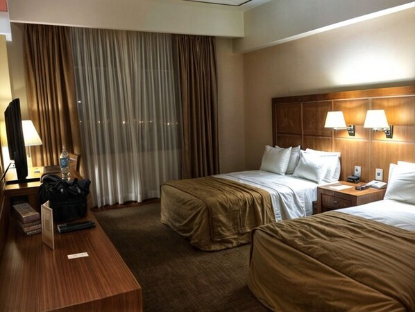 Una habitación de hotel con dos camas, un escritorio de madera, un televisor y una ventana con cortinas.