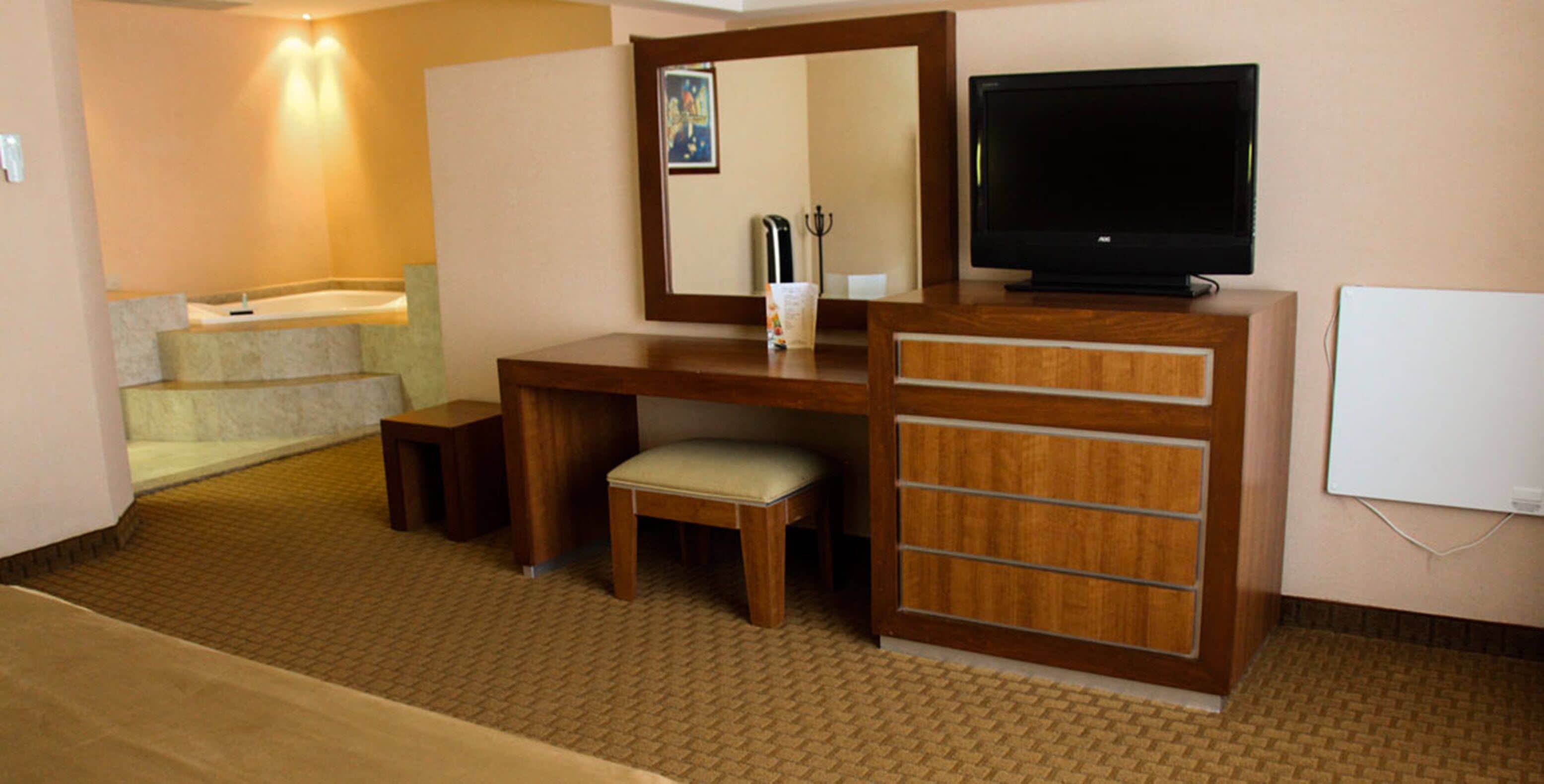 Een hotelkamer met een houten bureau, een televisie, een kleine stoel en een bank.